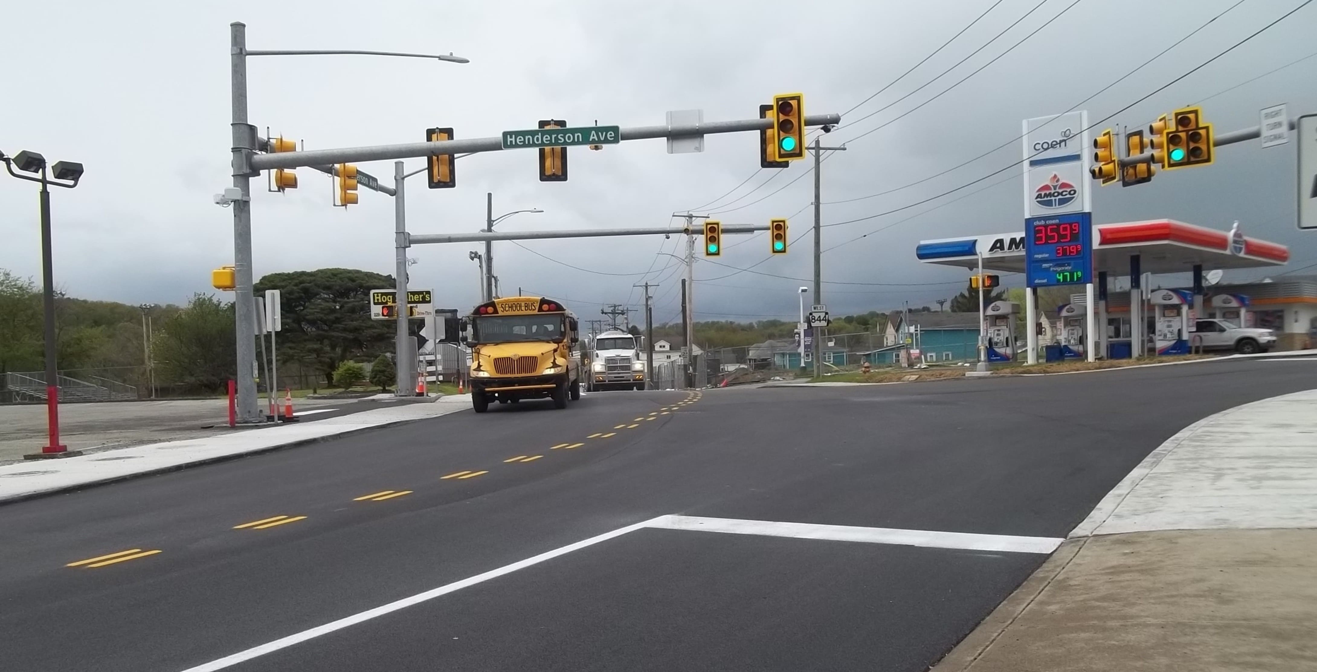 A school bus navigates its way through an intersection with traffic lights and a gas station to the right in the background.
